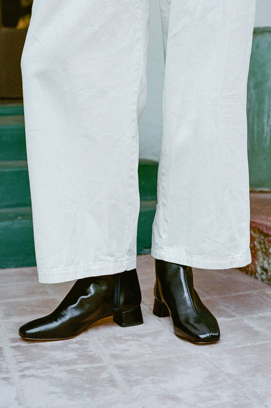 A person wearing white pants and black leather boots with a square toe and low heel.