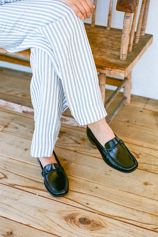 Person wearing black loafers and white striped pants sitting on a wooden staircase.