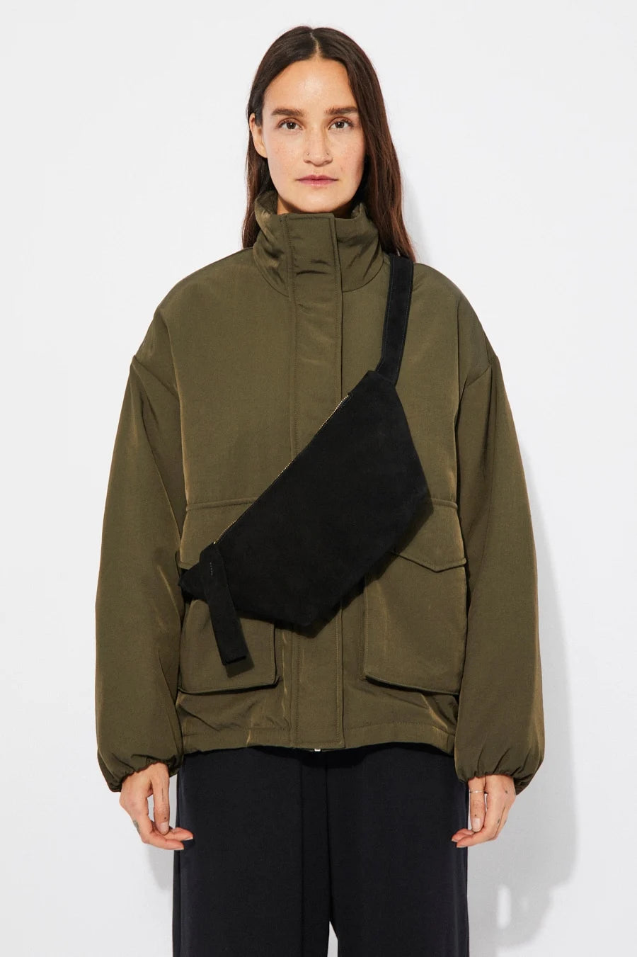 Person wearing a green jacket with a black suede cross body bag over one shoulder on a white background