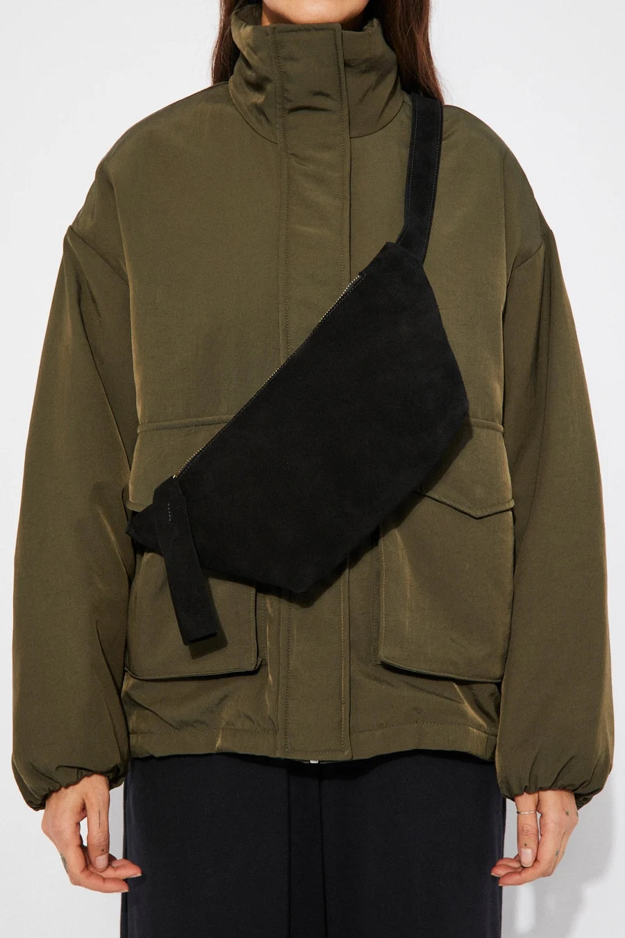 Person wearing a black suede cross body bag with a green jacket over a white background