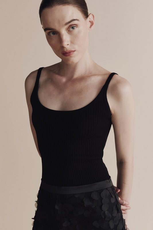Woman wearing a black tank top against a neutral background