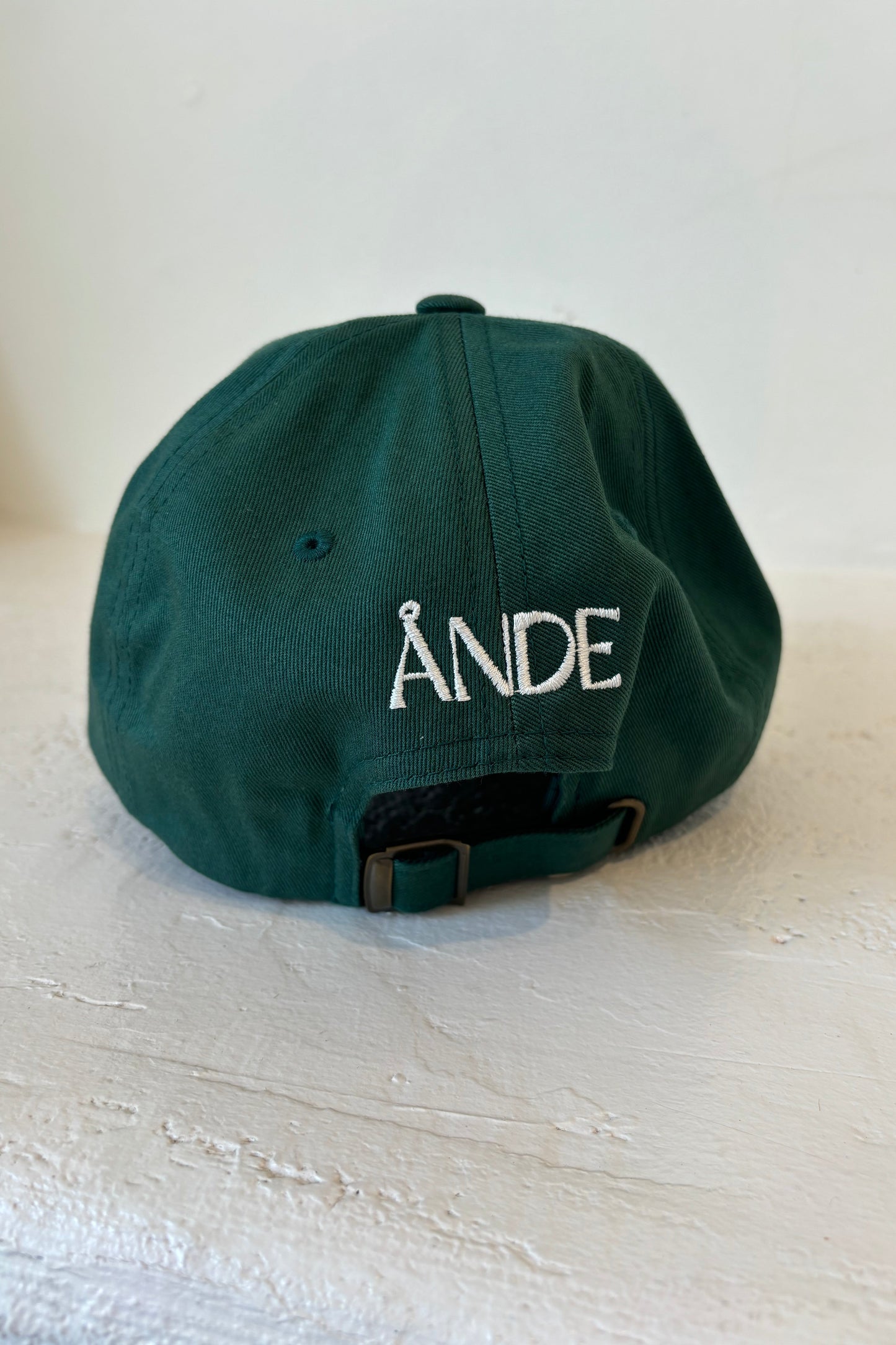A green baseball cap with a white embroidered ÅNDE on the back