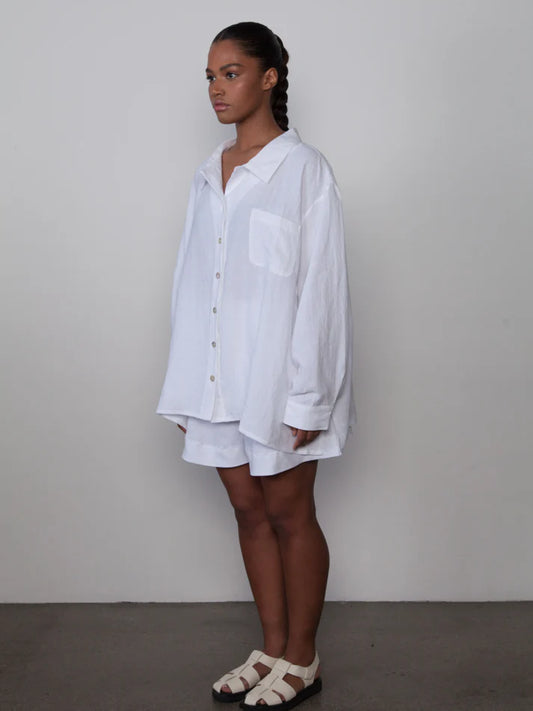 Person wearing a white oversized shirt and shorts against a plain background