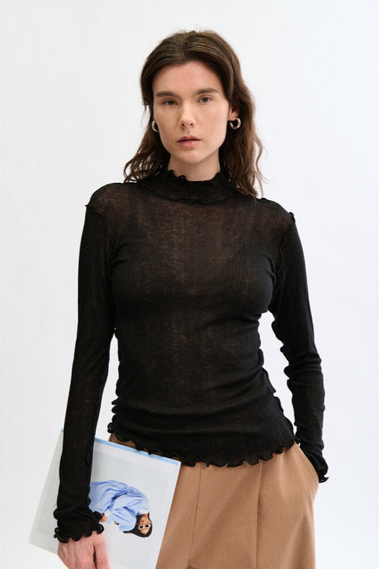Woman wearing a black long-sleeve top with sheer sleeves on a white background
