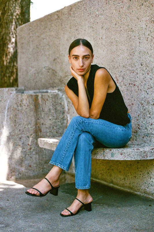 Woman sitting on a stone bench wearing a black top and blue jeans.