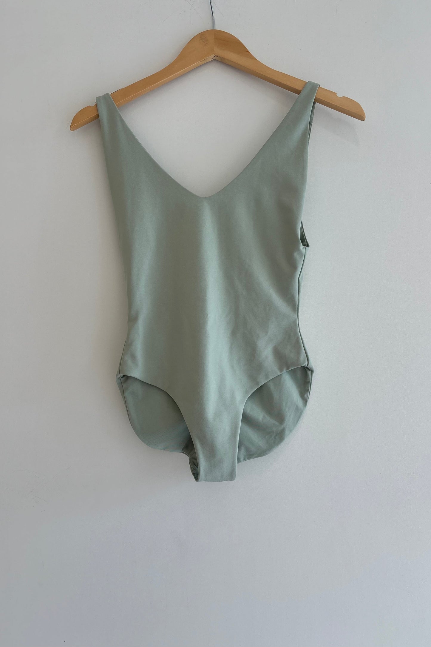 Green bodysuit on a wooden hanger against a white wall