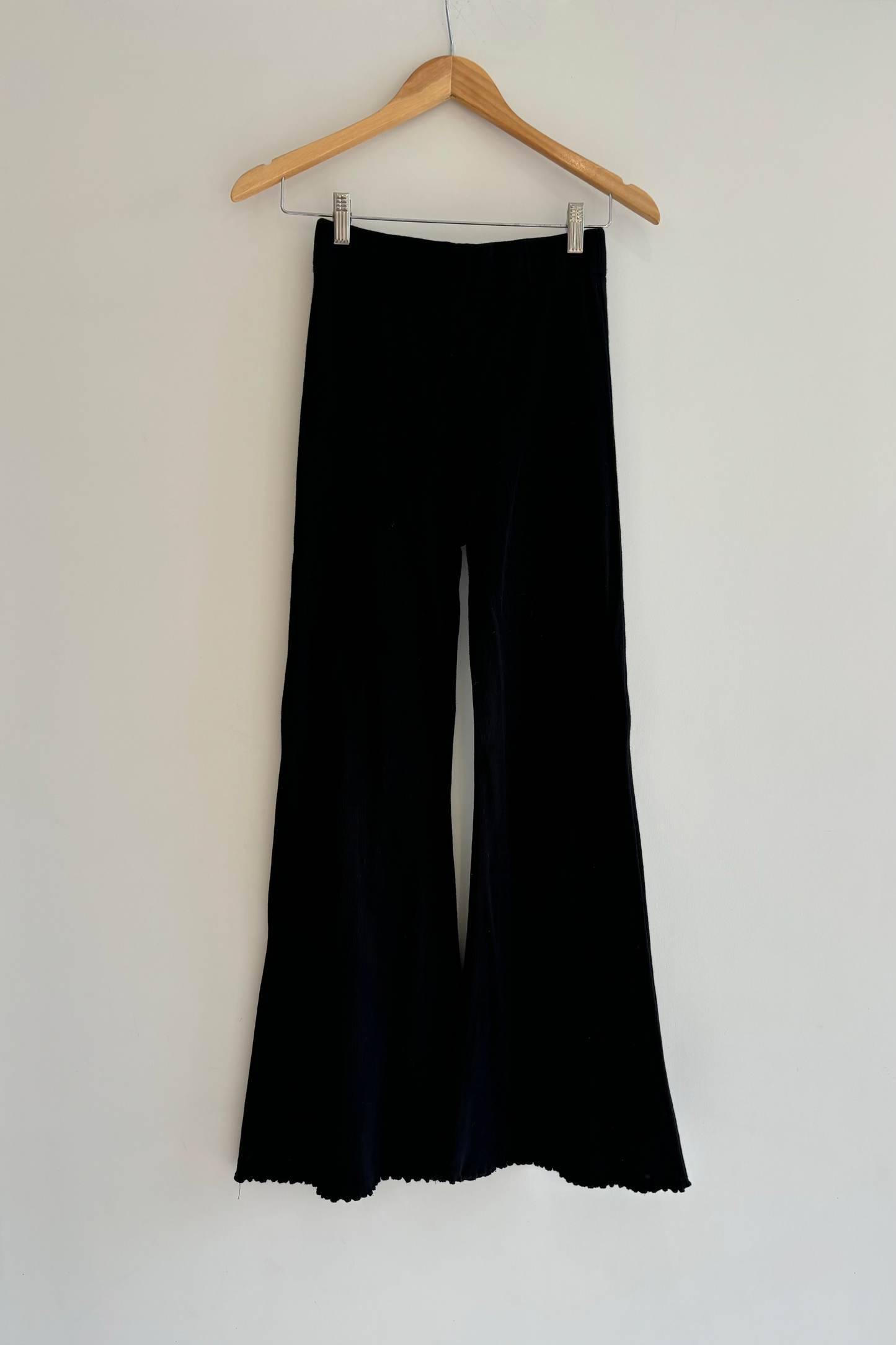 Black pants hanging on a wooden hanger against a white wall