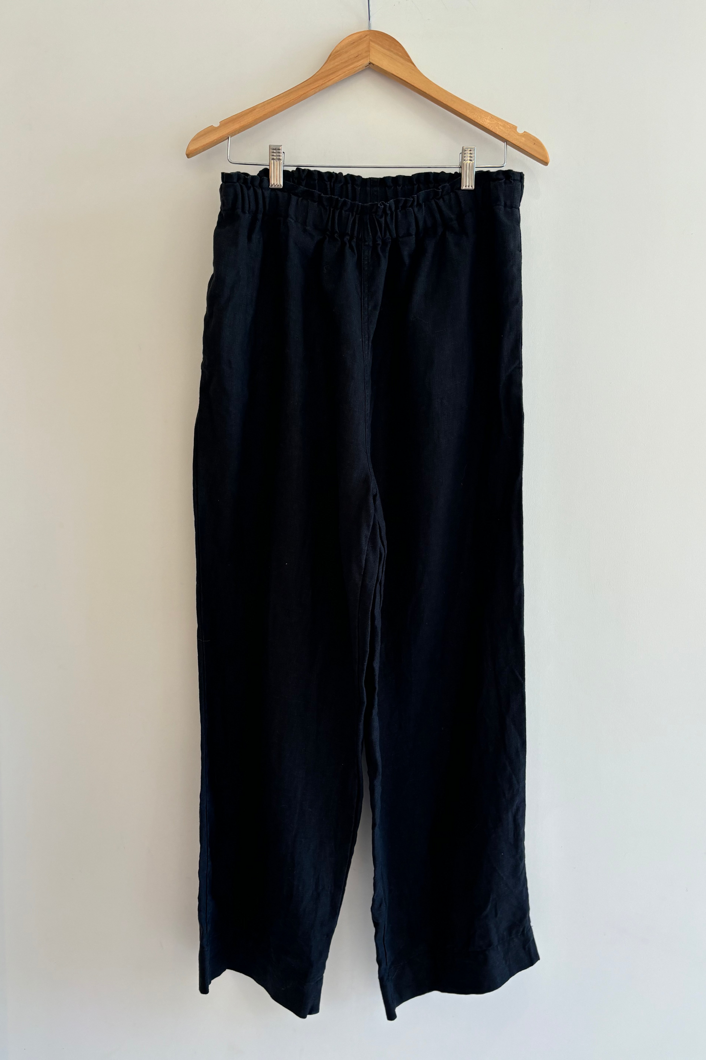 Black pants hanging on a wooden hanger against a white wall