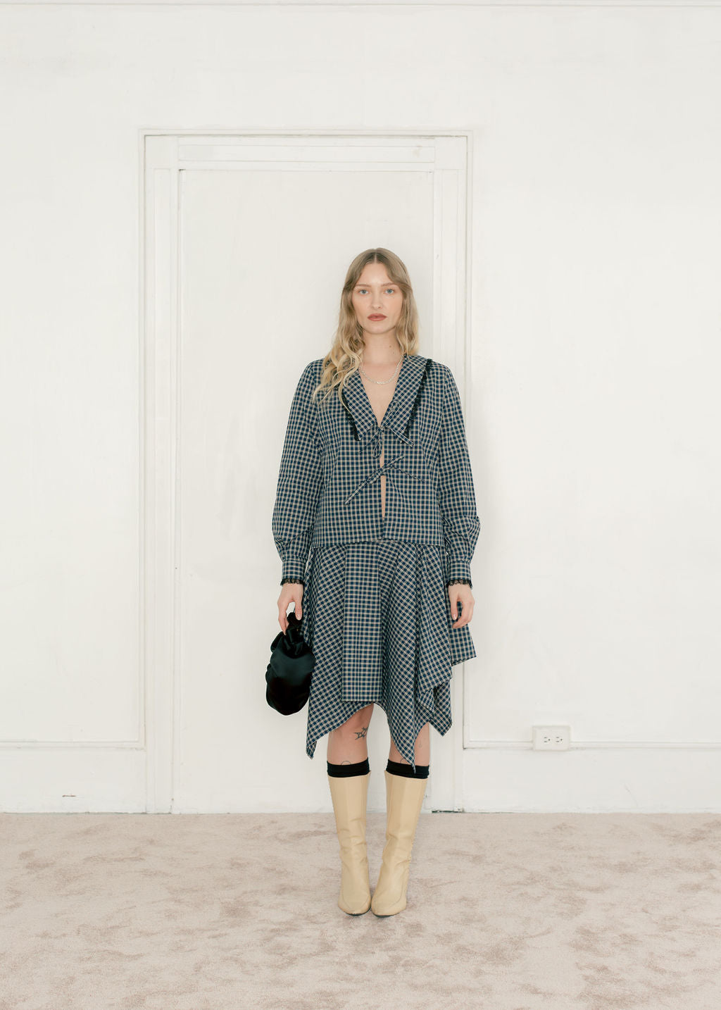 Woman wearing a checkered dress with beige boots in a minimal indoor setting