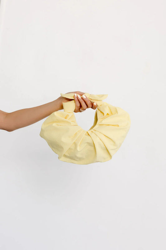 A hand holding a yellow, croissant-shaped, traditional Japanese folding handbag against a white background.
