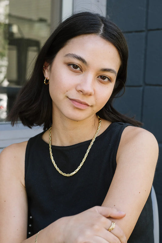 Woman wearing a black sleeveless top and gold necklace with a blurred background