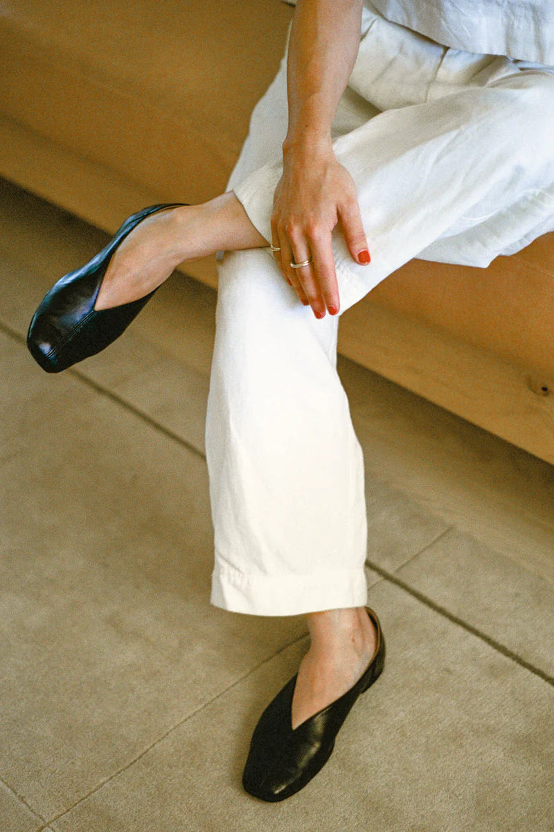 Person wearing white pants and black leather slipper shoe with central seam and tulip shaped upper with squared-off toe and 3/4" heel.