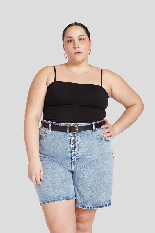 A person wearing a black tank top and light blue denim shorts with a belt.