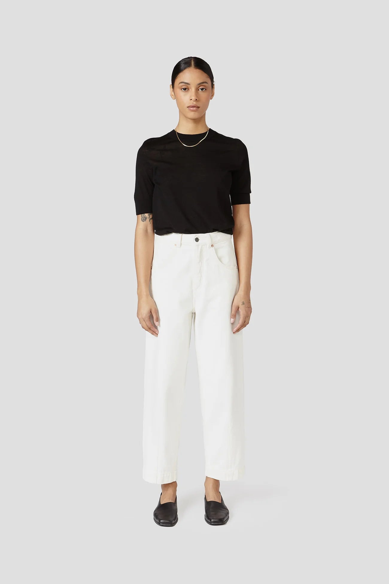 Person wearing a black top and white pants on a white background