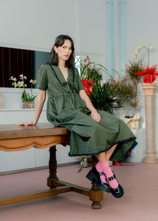 Woman in a green dress sitting on a wooden bench with plants in the background