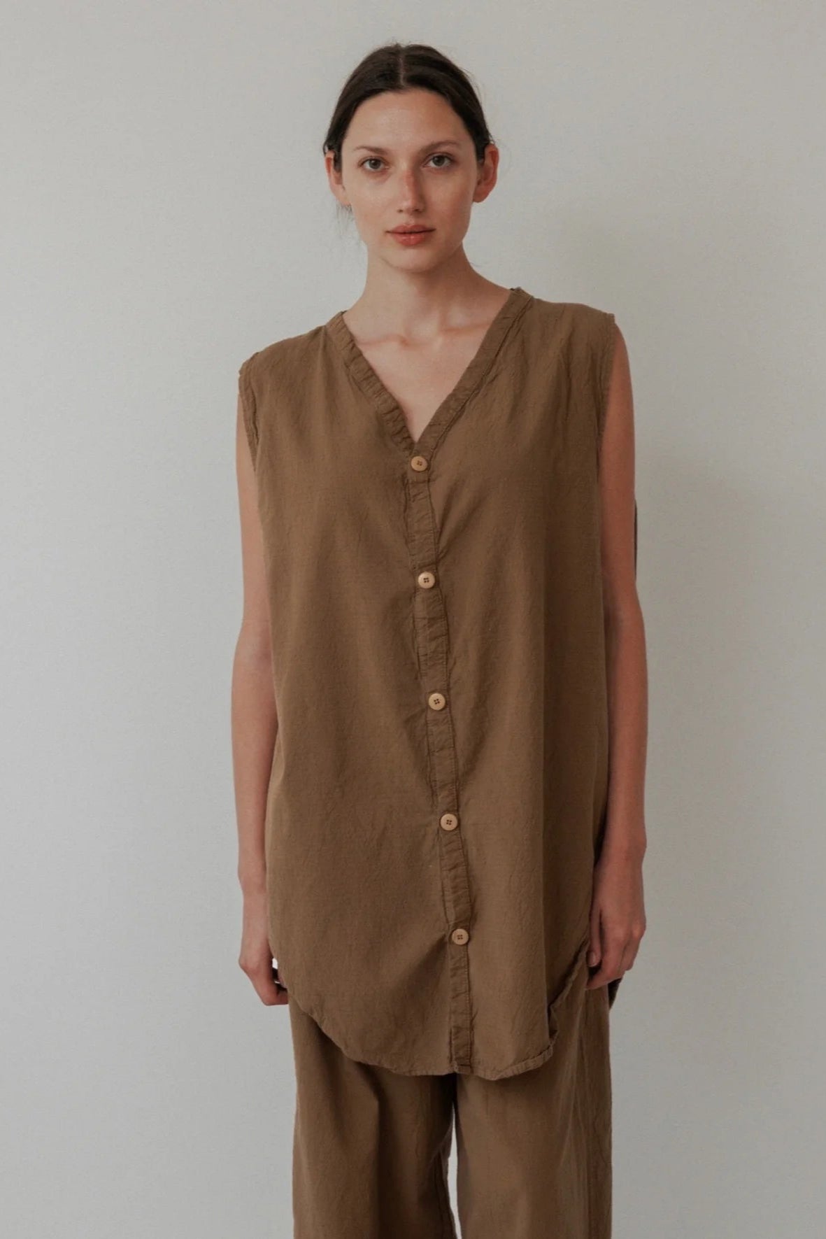 Woman wearing a brown sleeveless top and pants against a plain background