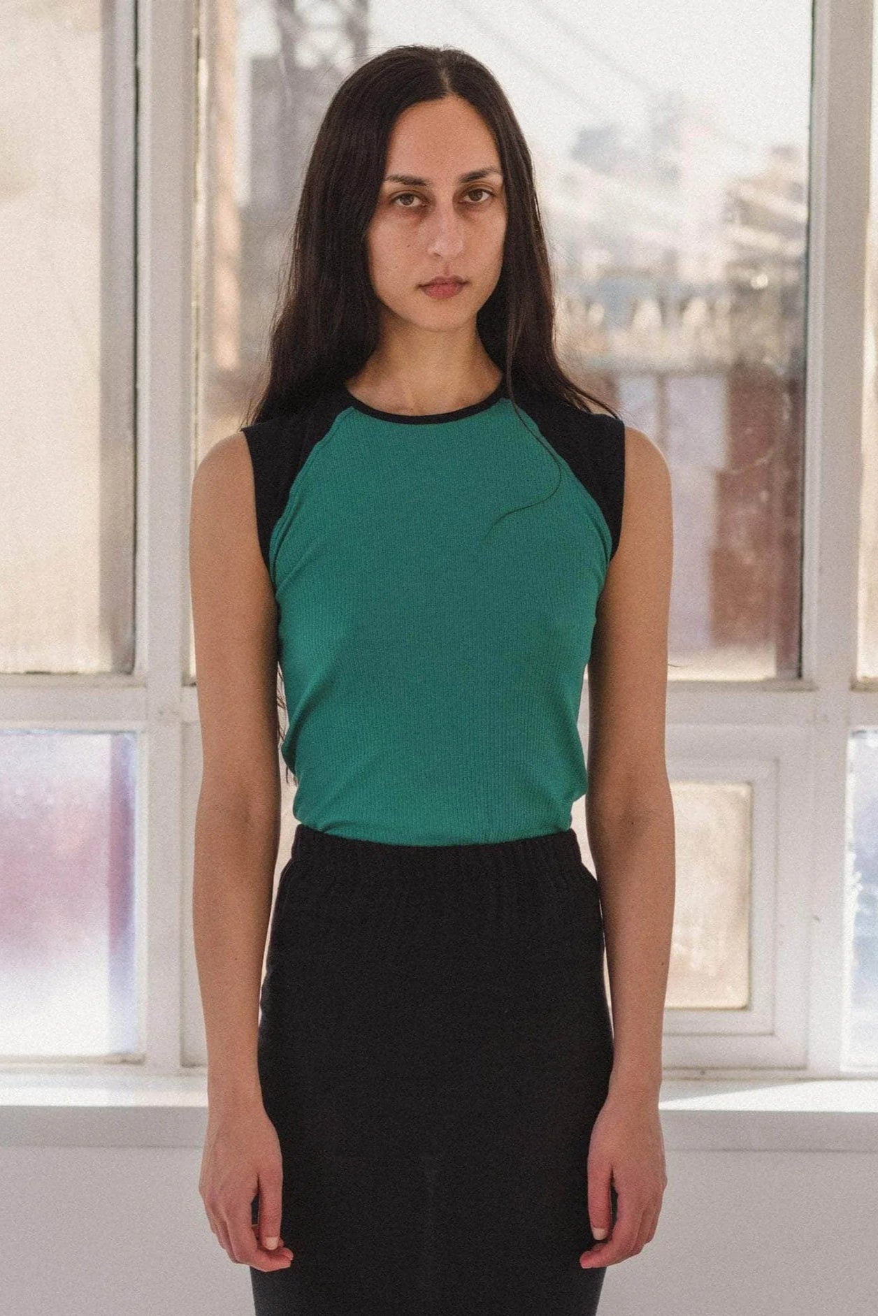 Woman wearing a green and black sleeveless top in front of a window