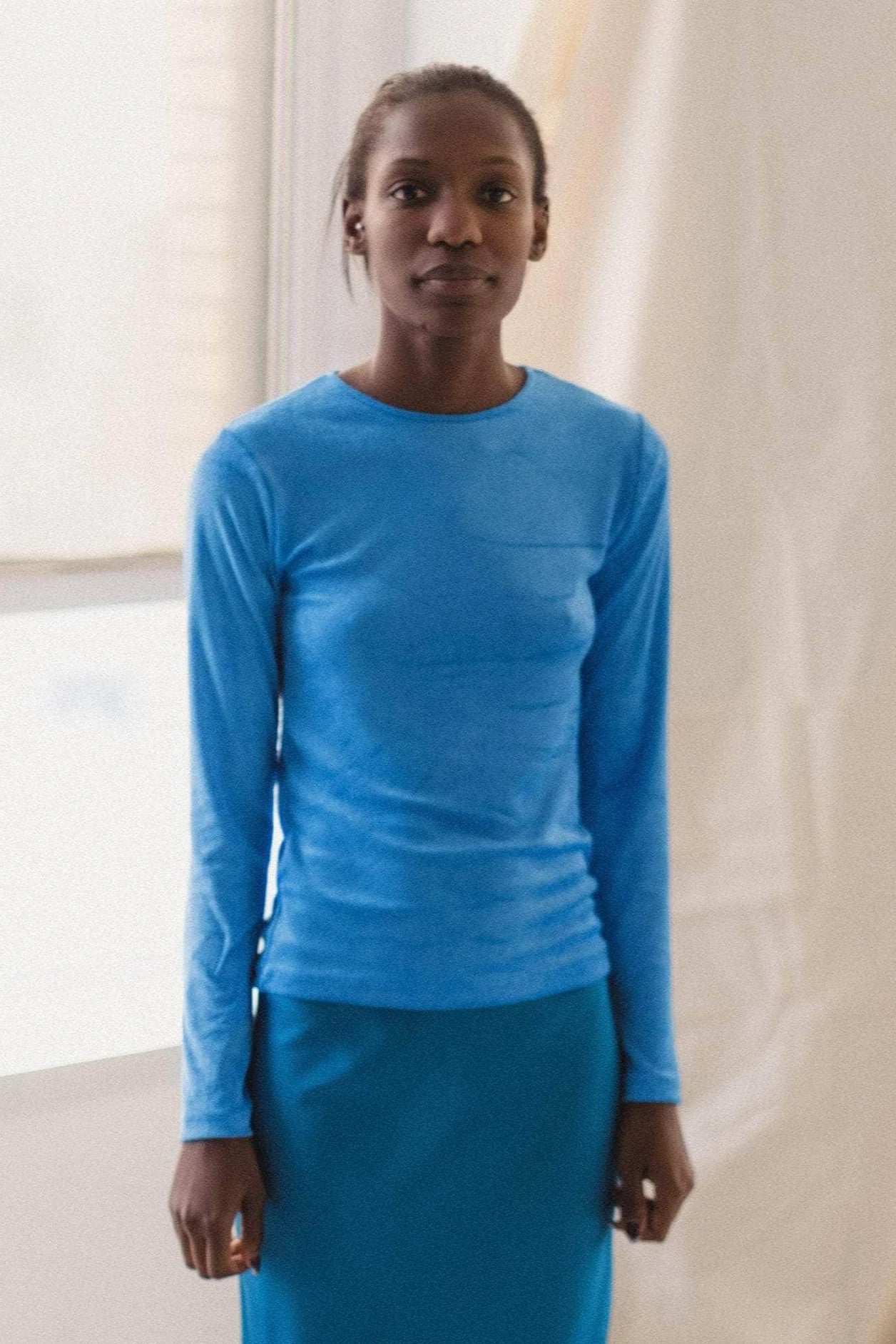 Person wearing a blue long-sleeve top and skirt against a neutral background