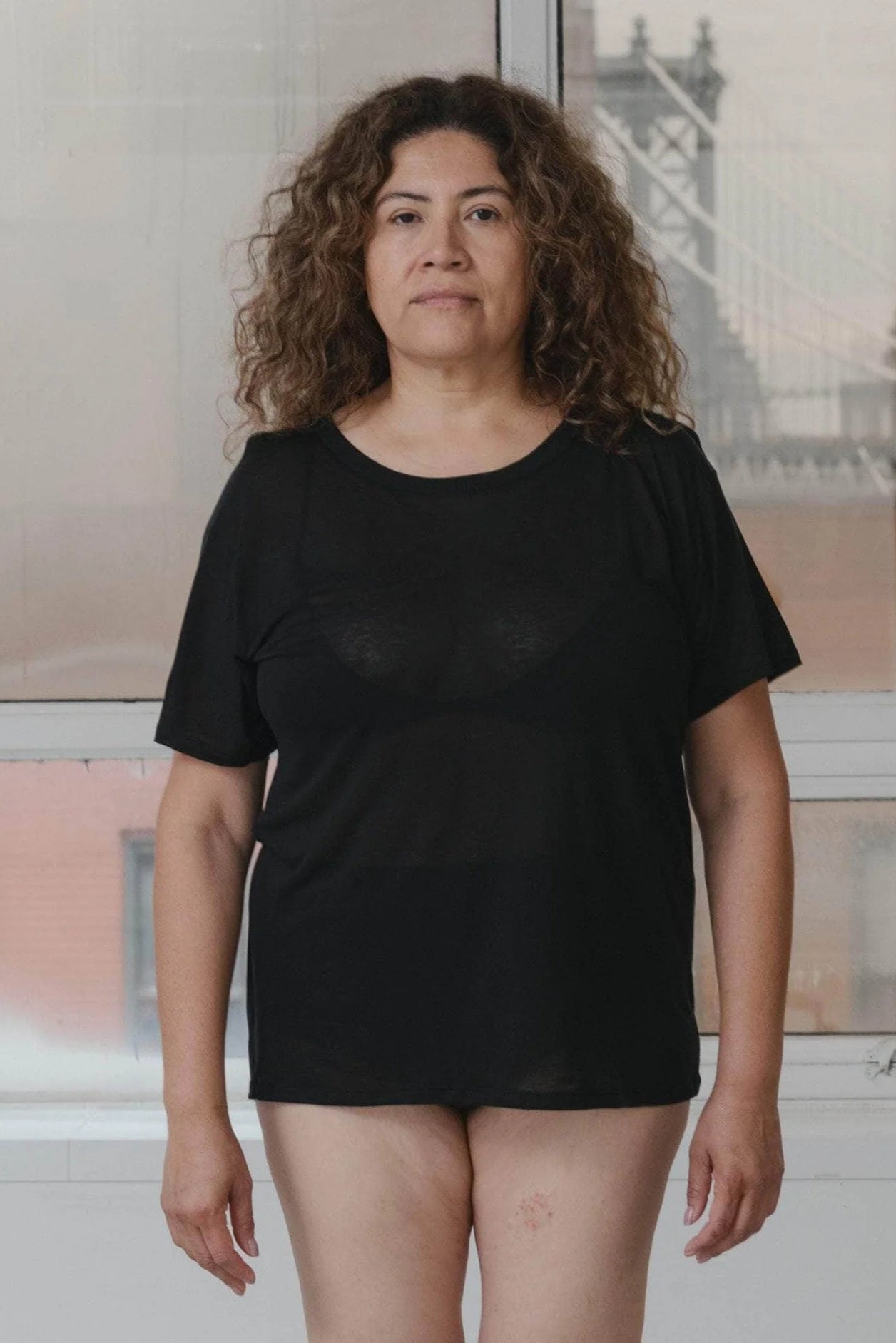Person wearing a black t-shirt standing in front of a window with a blurred cityscape.