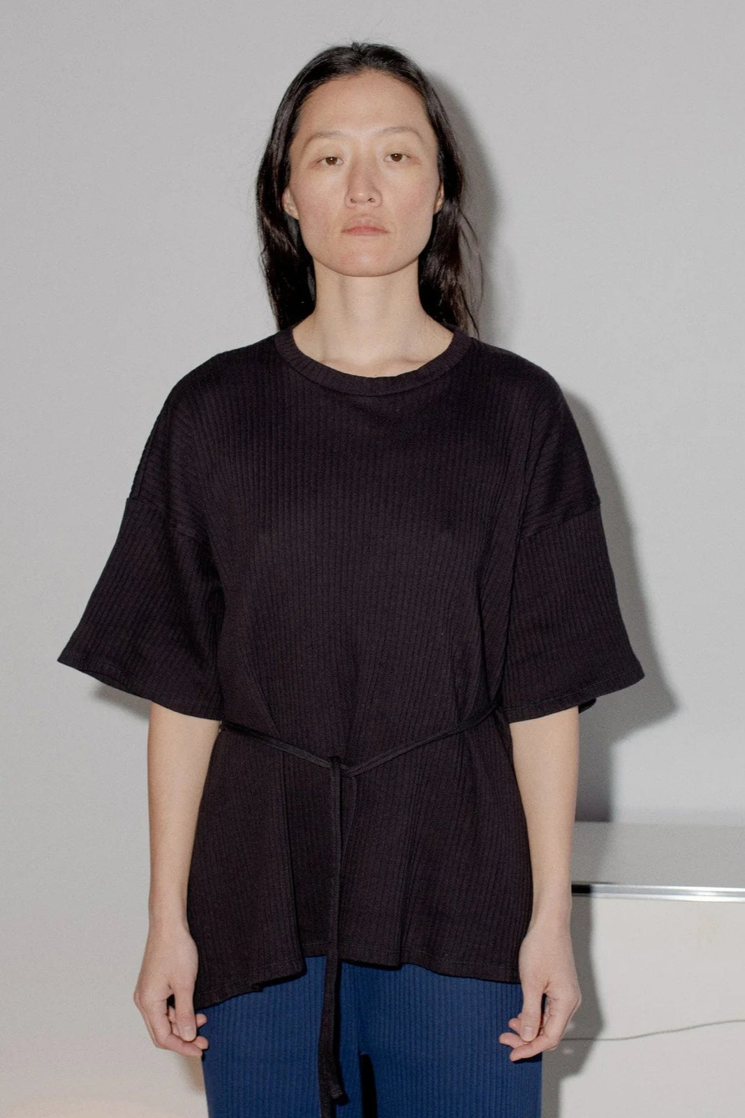 A person wearing a black ribbed cotton jersey short sleeve wrap top with a crewneck and oversized fit.