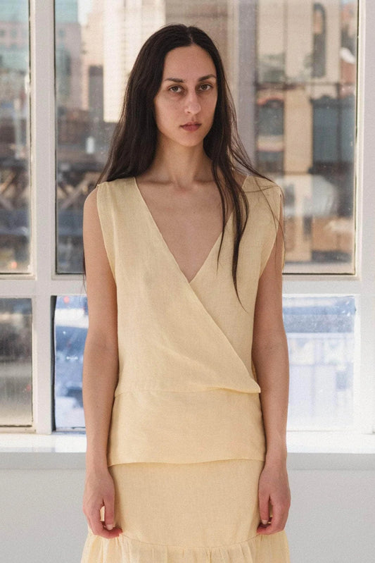 Woman wearing a light yellow top standing in front of large windows with a cityscape view.