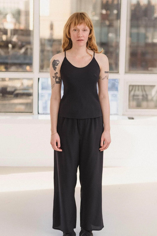 Person wearing a black outfit standing in a modern indoor setting with large windows.