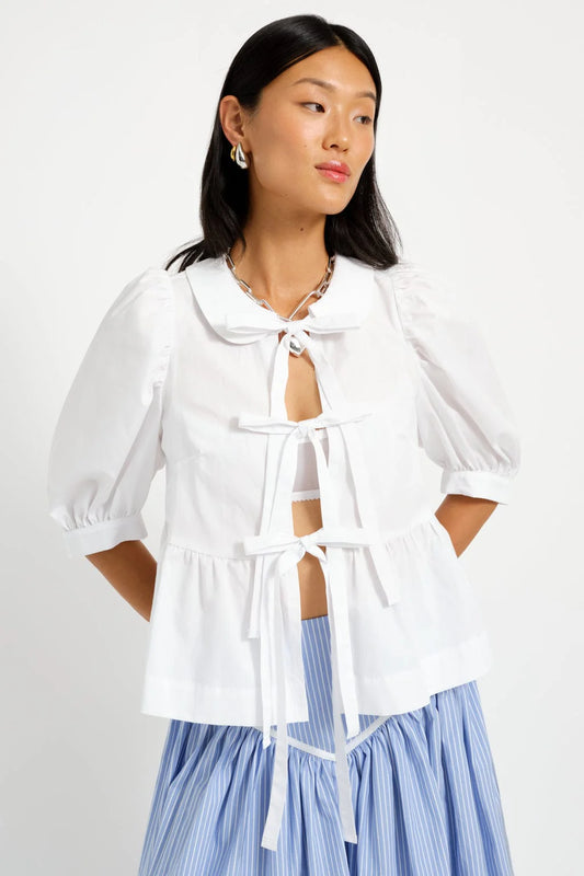 A woman wearing a white Georgie Blouse with three bows tying up the front, made of cotton, in Canada.