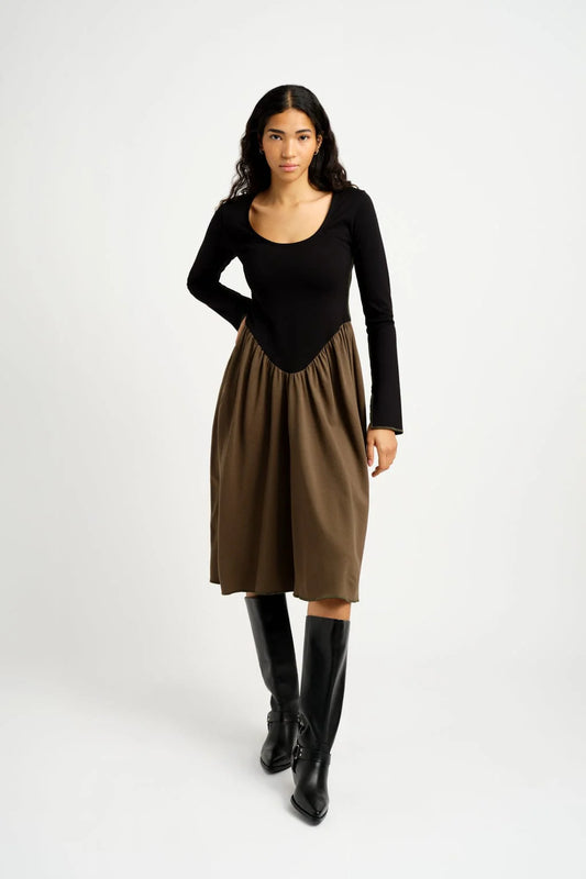 A model wearing a Joan Dress in black and khaki, with long sleeves and a basque waistline, paired with black boots.