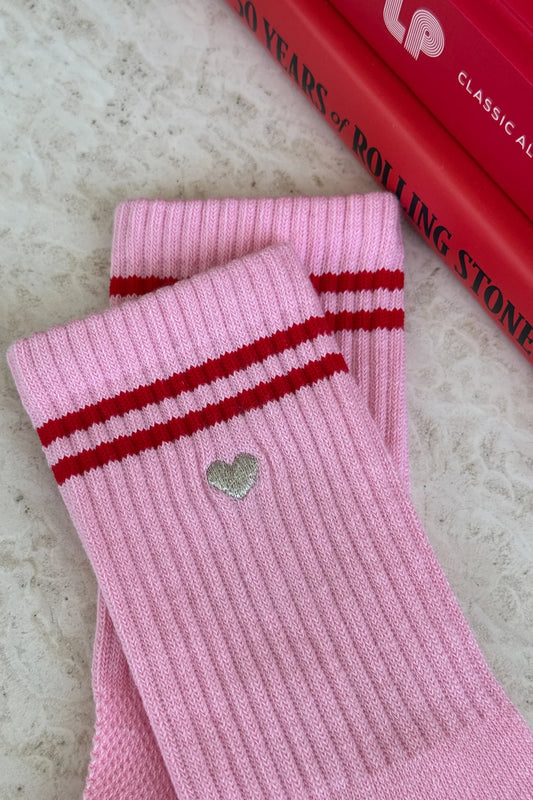 Close-up of Le Bon Shoppe Embroidered Boyfriend Socks in amour pink showing embroidered silver heart detail below red double stripe on pink ribbed cotton, laid on a marble surface