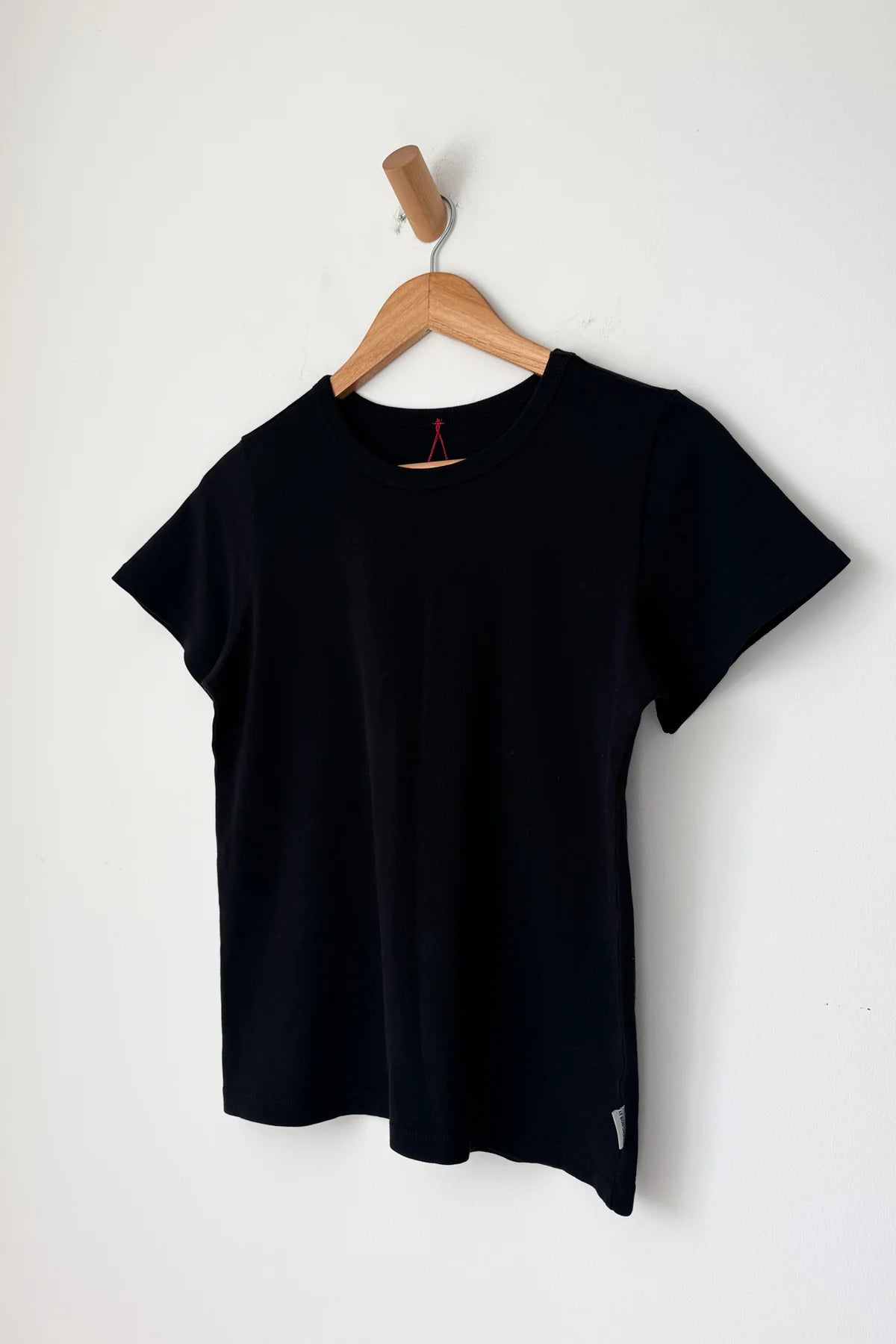 Le Bon Shoppe Go-To Tee in true black on a wooden hanger against a white wall, showing relaxed longer length silhouette, crew neck and short sleeves