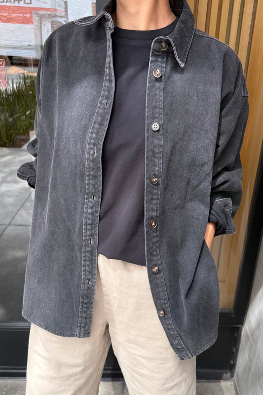 Close-up of Le Bon Shoppe Theo Jacket in black denim showing button front placket and contrast stitching, layered over a black tee with cream trousers