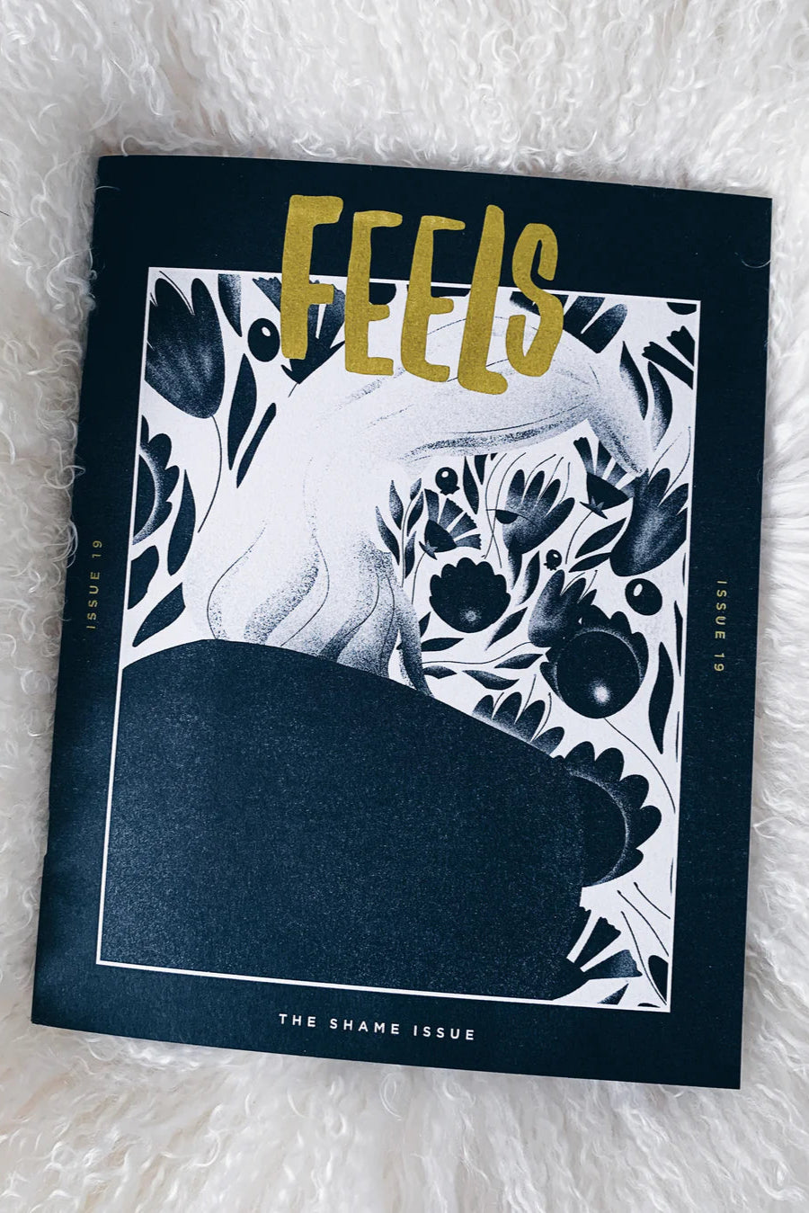 A magazine cover of 'FEELS' with a black and white floral design and text 'THE SHAME ISSUE'.
