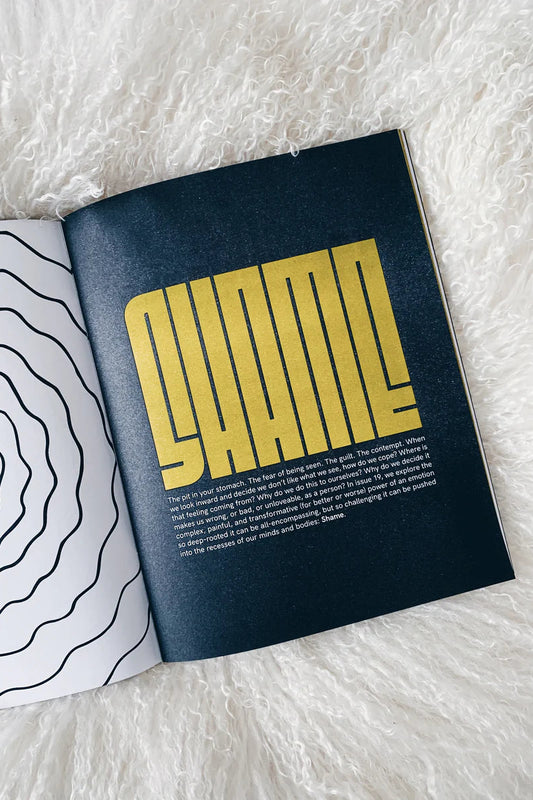 An inside page of a magazine with the words SHAME illustrated onto it in yellow type on a dark navy background