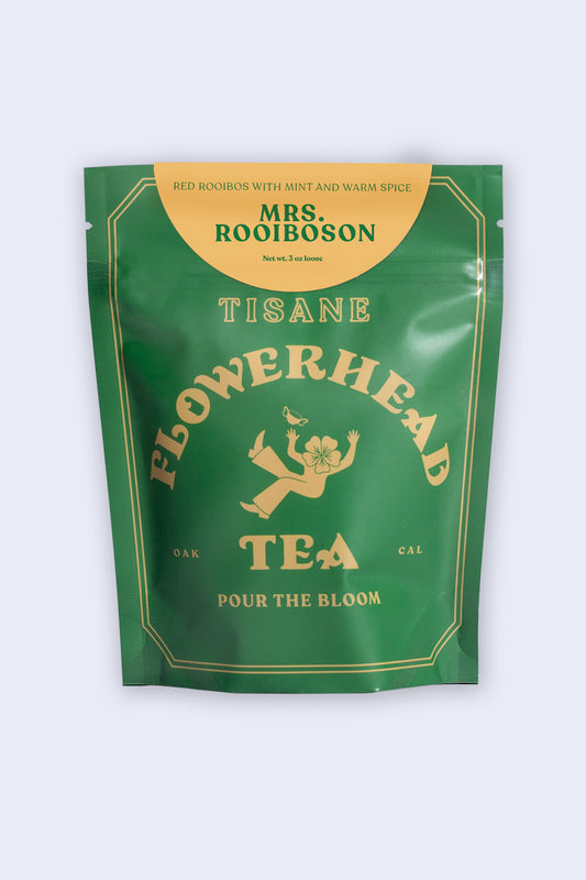 A packaged tea product labeled 'Mrs. Rooiboson' by Flowerhead Tea, featuring imagery of a rooibos plant and text describing the product as a rooibos blend with spices.