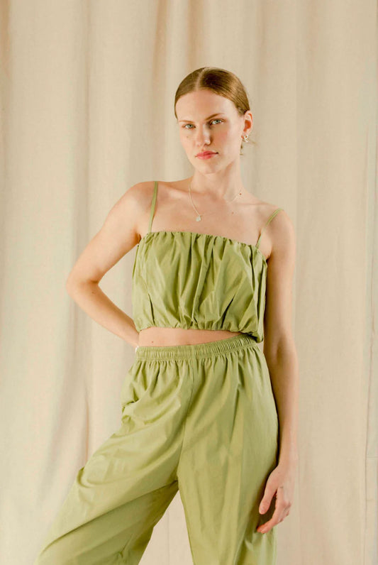 A person wearing a green Yara Crop Top with spaghetti straps and a gathered bust detail, paired with matching green pants.