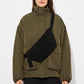 Person wearing a green jacket with a black suede cross body bag over one shoulder on a white background