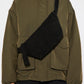 Person wearing a black suede cross body bag with a green jacket over a white background