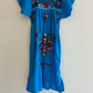 Blue dress with colorful embroidery on a hanger against a beige wall