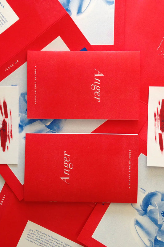 A collection of red zines titled 'Anger' arranged on a surface with some white cards and printed materials featuring red marks or text.