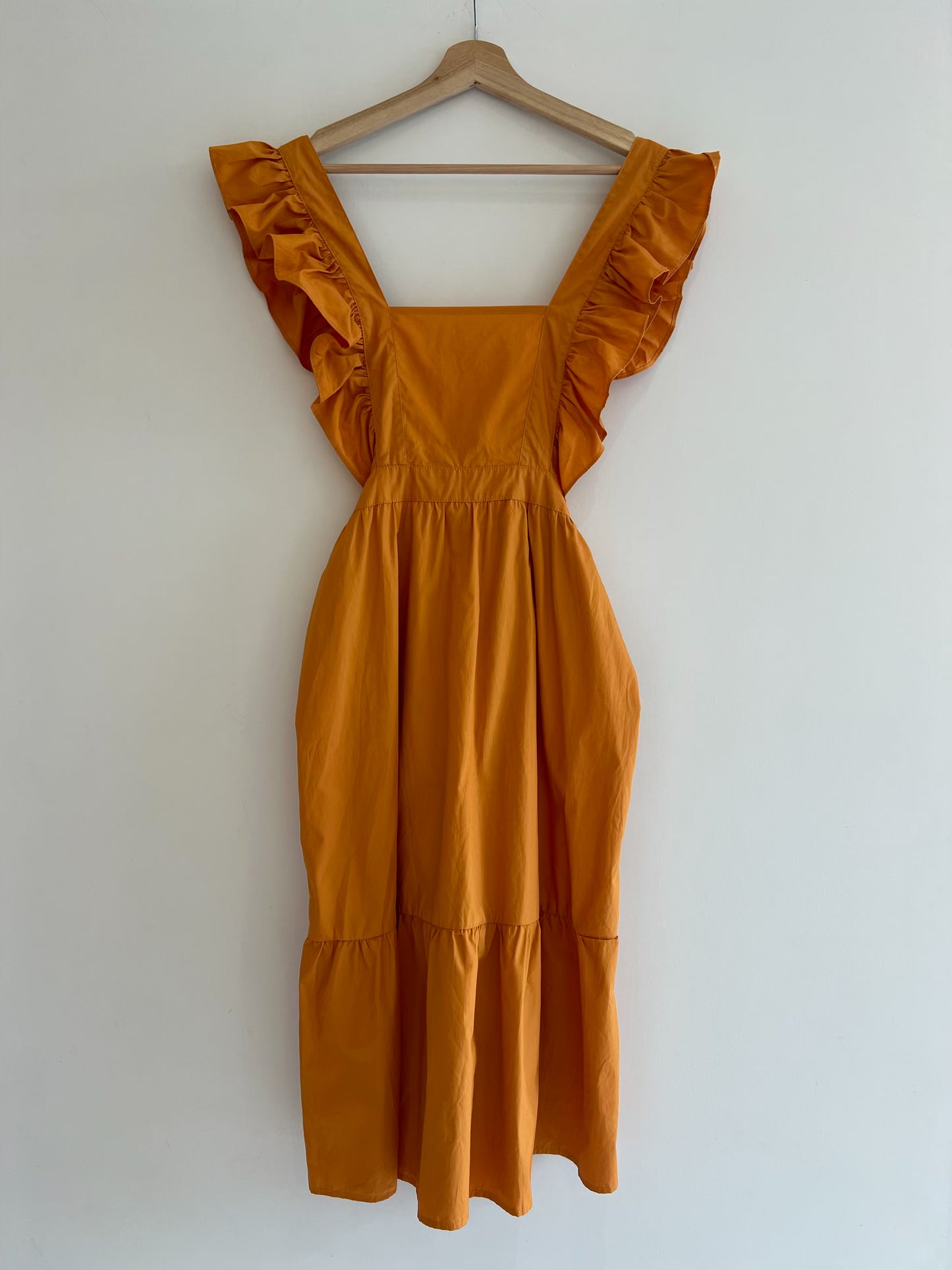 Mustard yellow dress with ruffled sleeves on a wooden hanger against a white wall