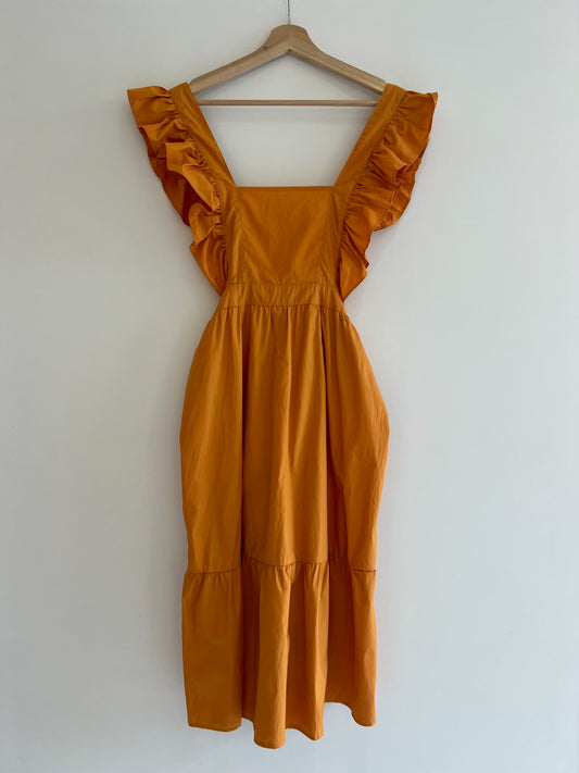 Mustard yellow dress with ruffled sleeves on a wooden hanger against a white wall