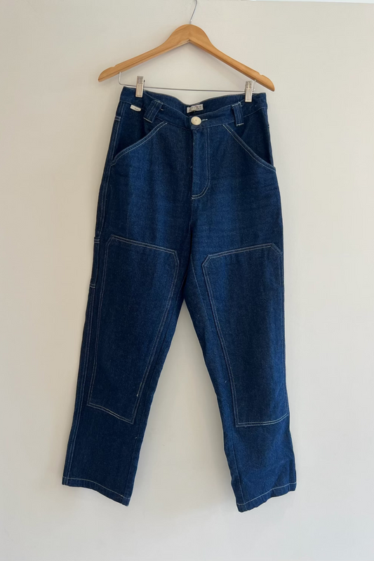 Blue jeans hanging on a wooden hanger against a white wall