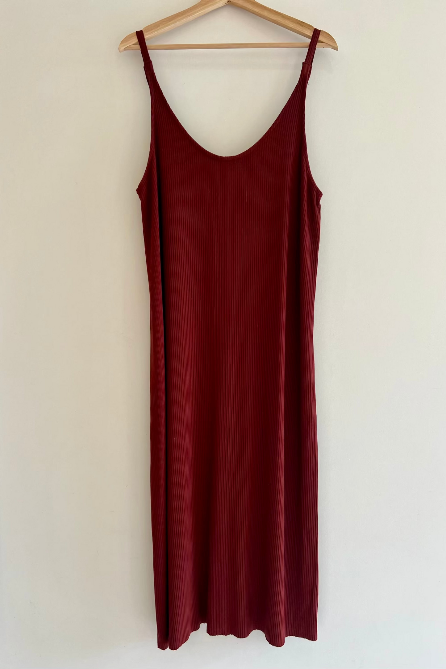 Maroon slip dress on a wooden hanger against a white background