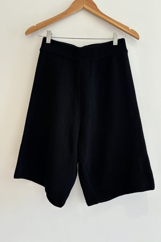 Black shorts on a wooden hanger against a white background