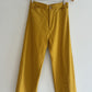 Mustard yellow pants on a wooden hanger against a white background