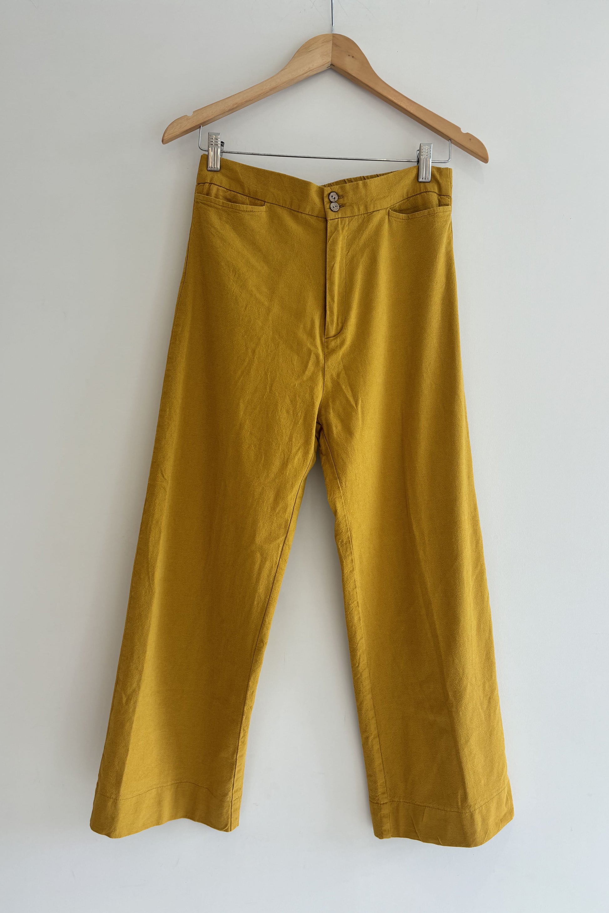 Mustard yellow pants on a wooden hanger against a white background