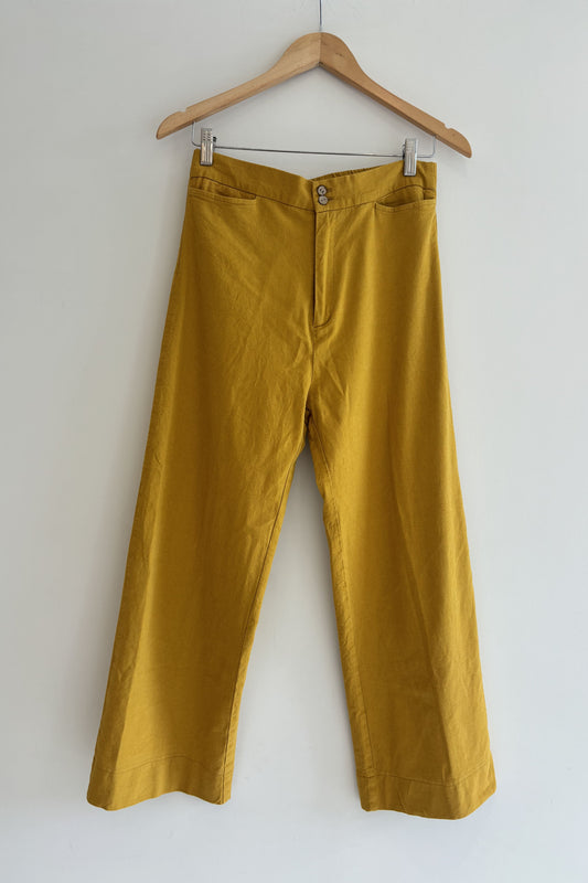 Mustard yellow pants on a wooden hanger against a white background