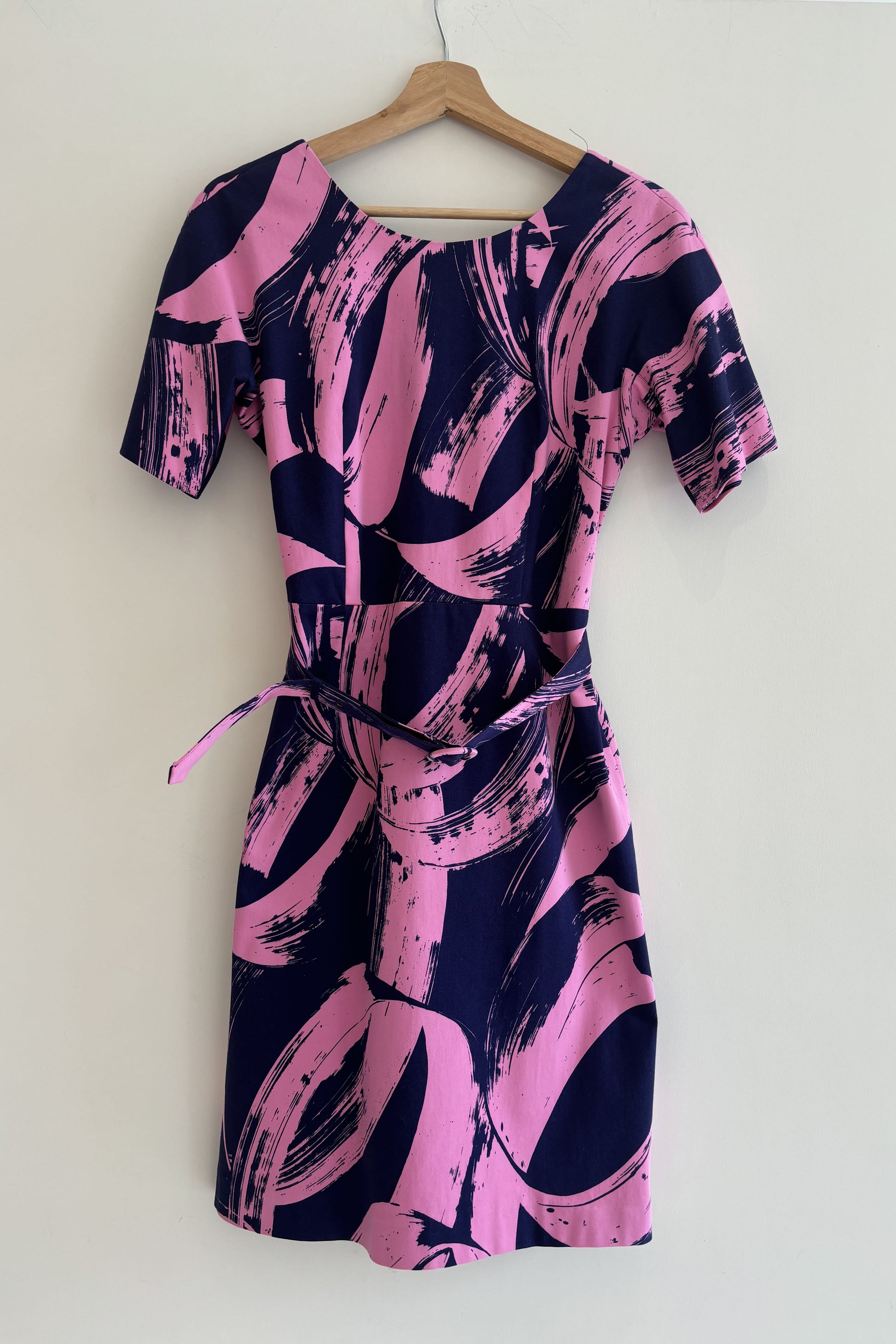Pink and navy abstract patterned dress on a hanger against a white background