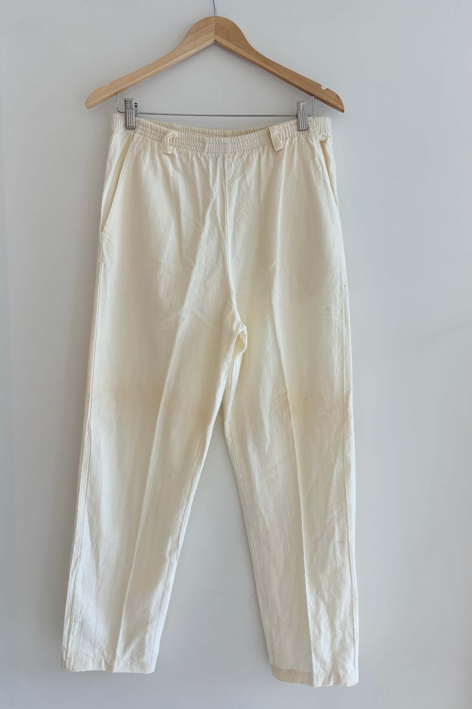 Beige pants hanging on a wooden hanger against a white wall