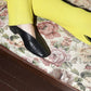Person wearing yellow pants and black leather slipper shoes with a central seam and tulip shaped upper. Features a squared-off toe and 3/4" heel.
